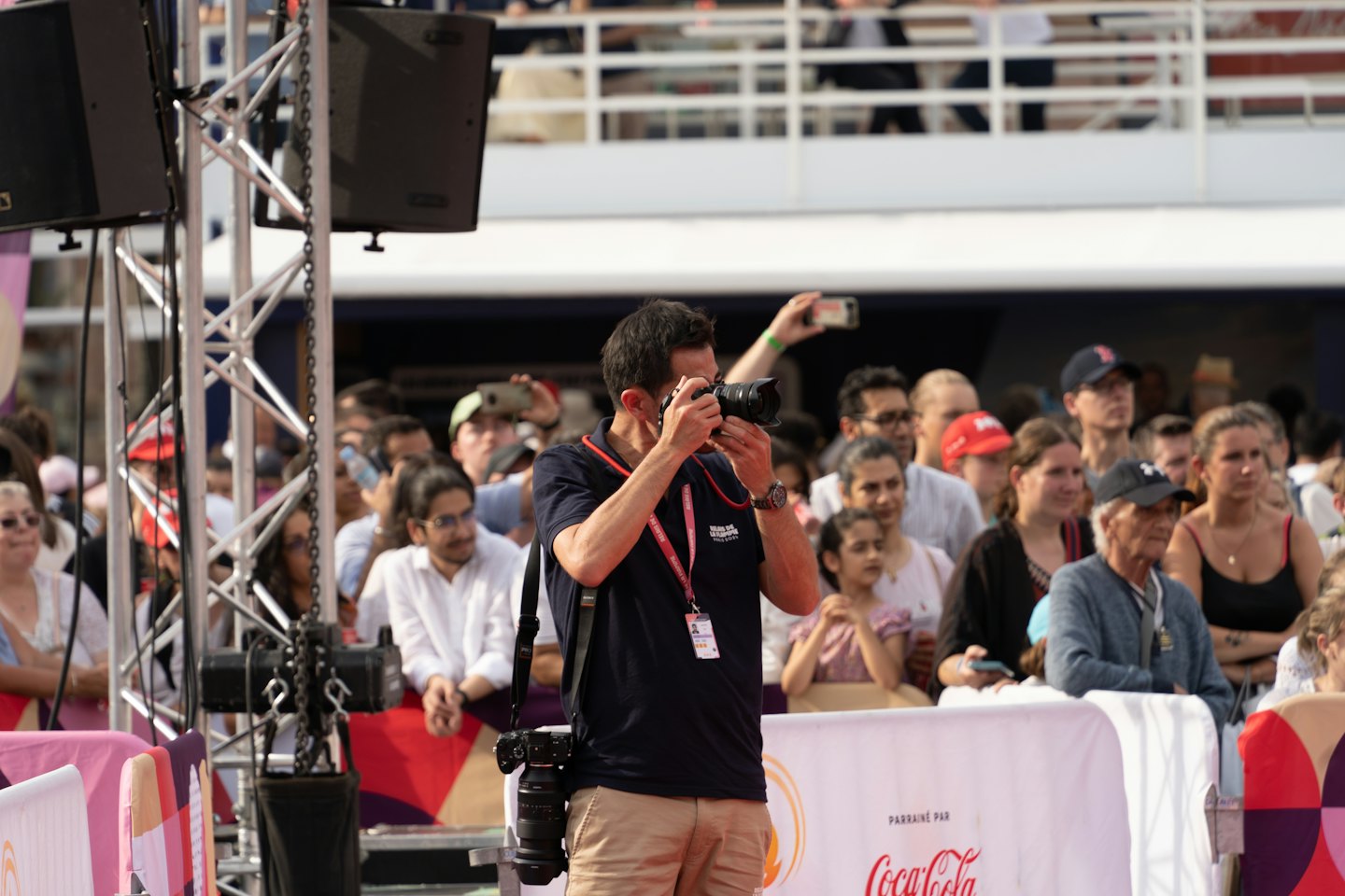 Uomo con fotocamera DSLR a un evento all'aperto dietro una barriera.